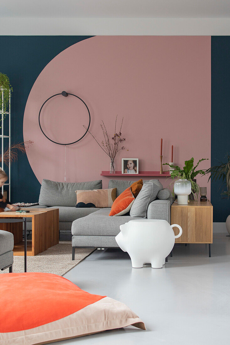 Wohnzimmer mit grauem Sofa und geometrischer Wandgestaltung in Rosa und Petrol