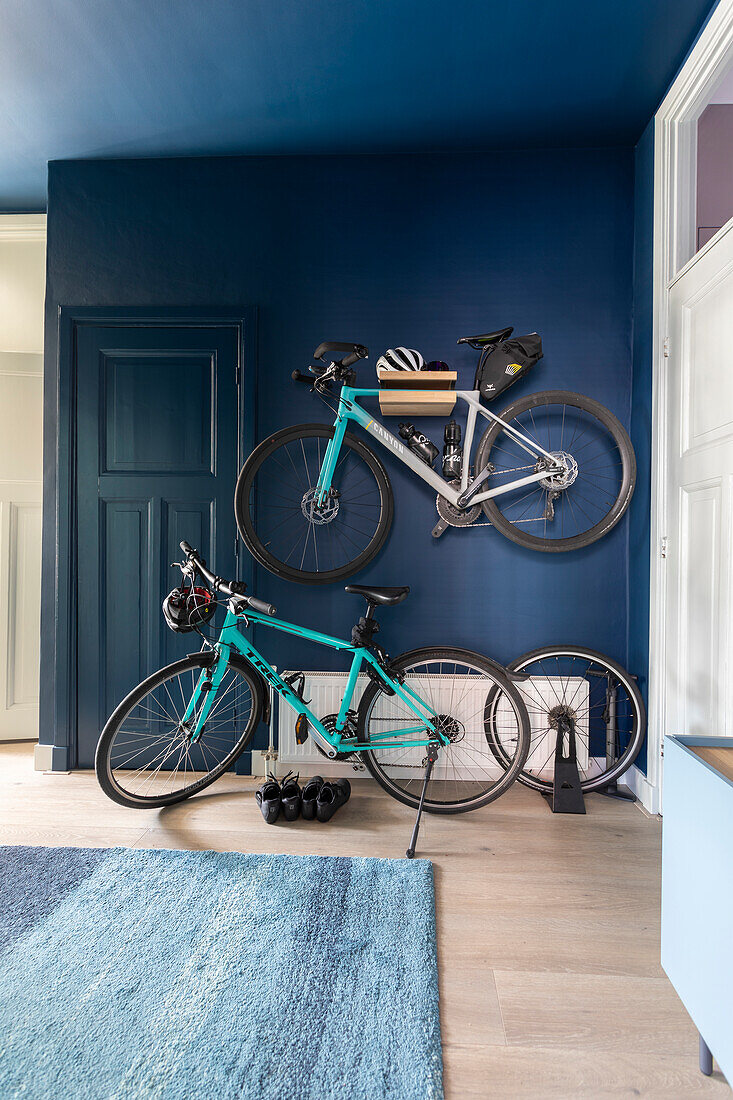 Fahrräder vor und an dunkelblauer Wand in Flur mit Holzboden und blauem Teppich