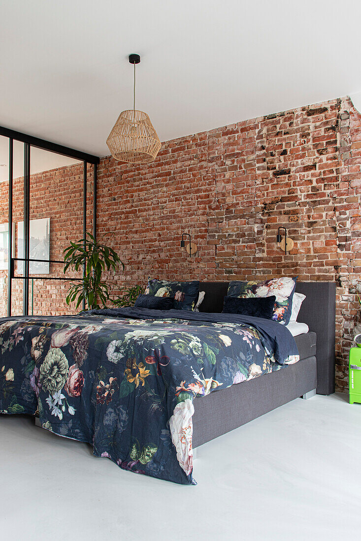 Bedroom with brick wall, bed with floral bed linen and rattan hanging lamp