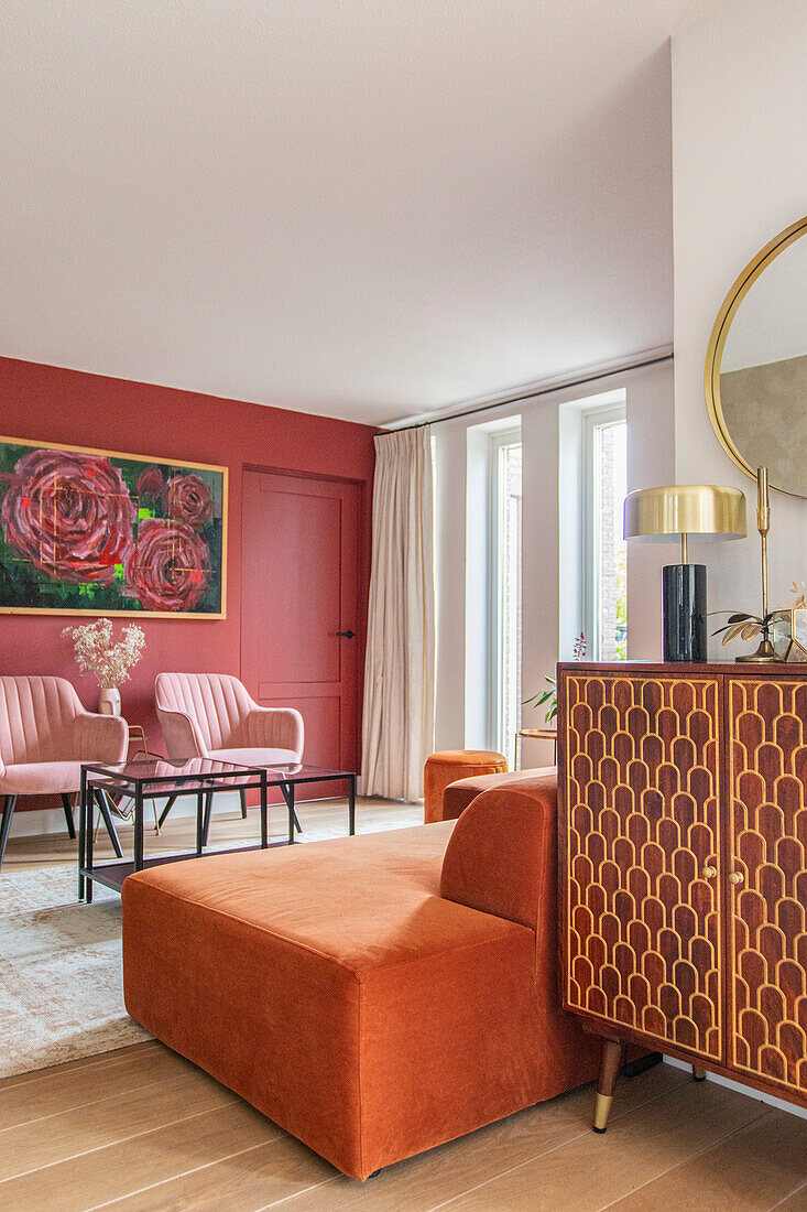 Living room with orange ottoman, pink armchairs and patterned wooden cabinet