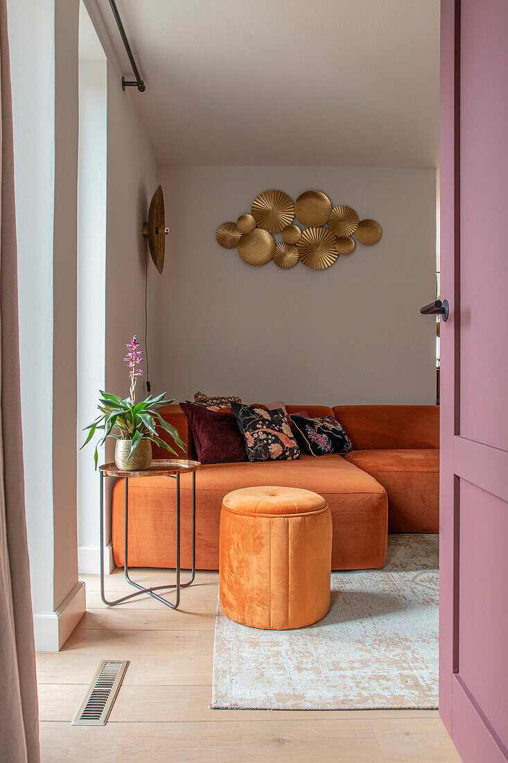 Living room with orange velvet sofa, golden wall art and plant