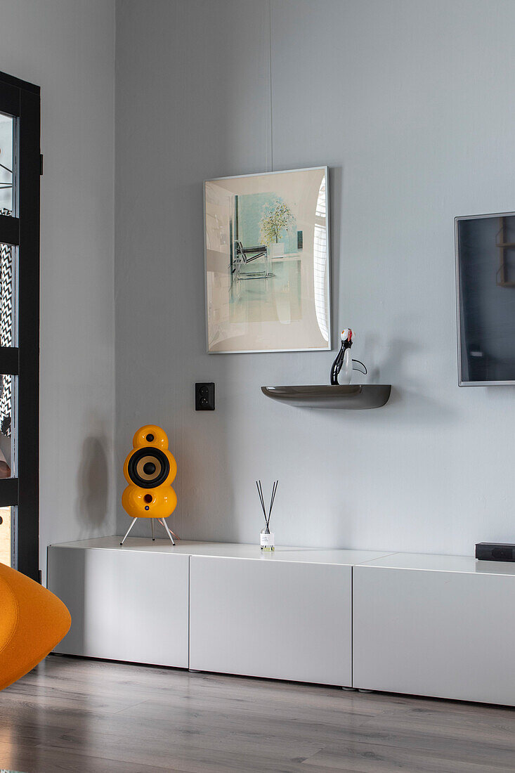 Minimalist living room with modern artwork and yellow speaker on white sideboard