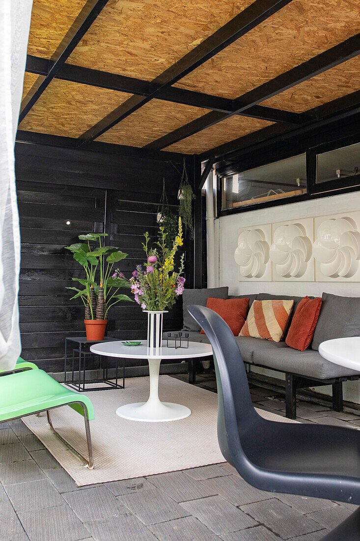 Überdachte Terrasse mit Lounge-Sofa, weißem Tisch und Pflanzen