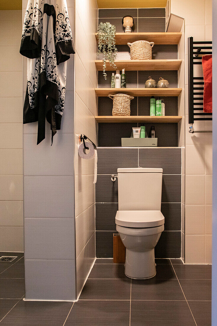 Toilette mit Wandregalen und weißen und grauen Fliesen