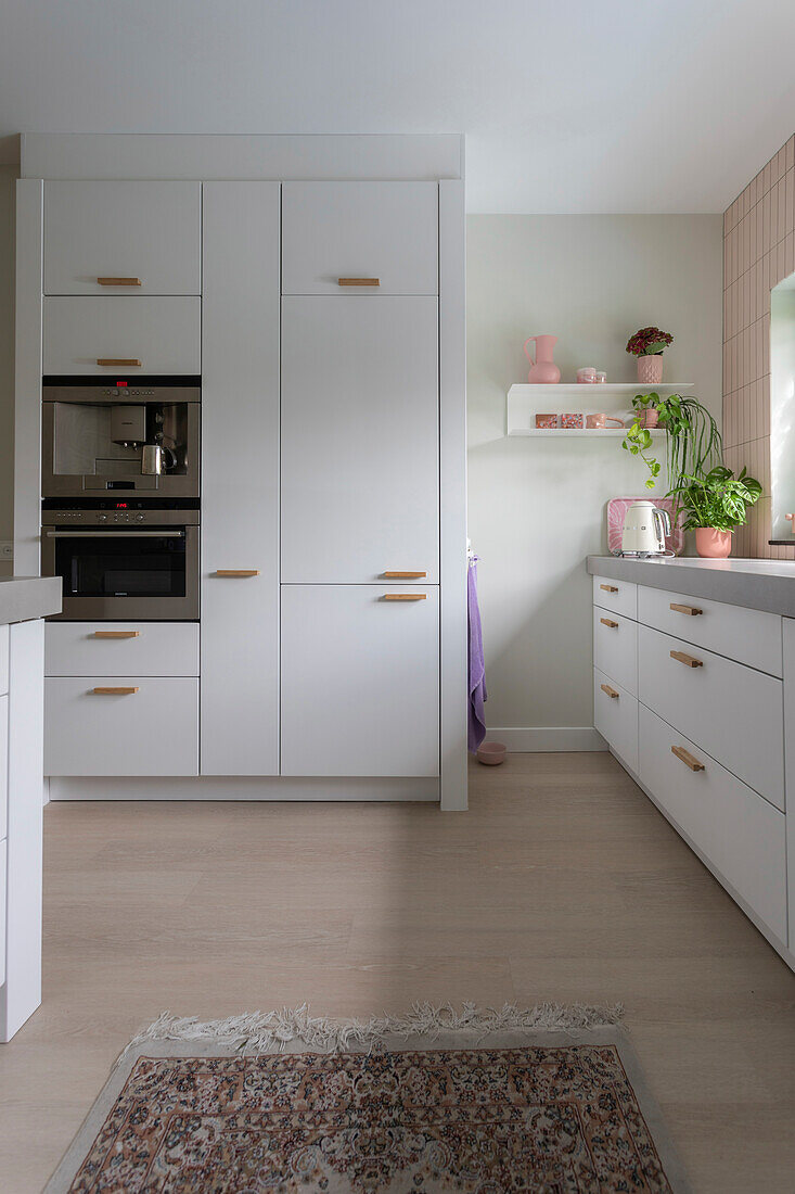 Modern white kitchen with built-in appliances, wooden handles and plants on the counter