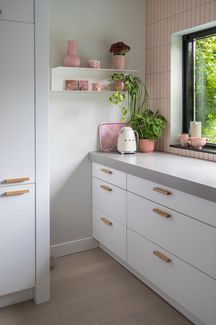 White kitchen with pink decorations and hanging shelves, view of the greenery