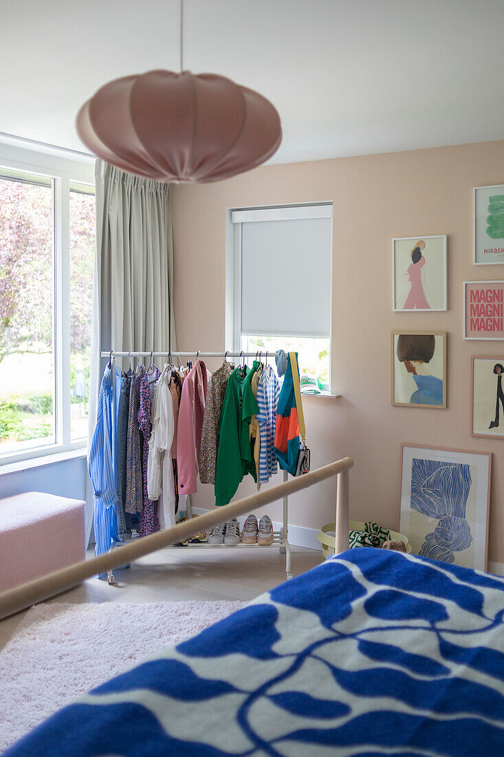 Bright bedroom with clothes rack, art on the walls and pink ceiling lamp