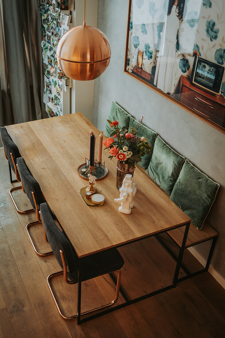 Dining room with wooden table, black chairs, green velvet cushions and copper pendant light