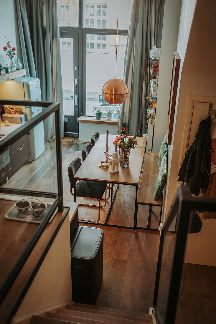 Dining area with wooden table, chairs and copper lamp by large windows