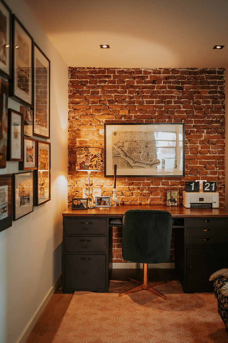 Arbeitsbereich mit schwarzem Schreibtisch und Bürostuhl vor Backsteinwand