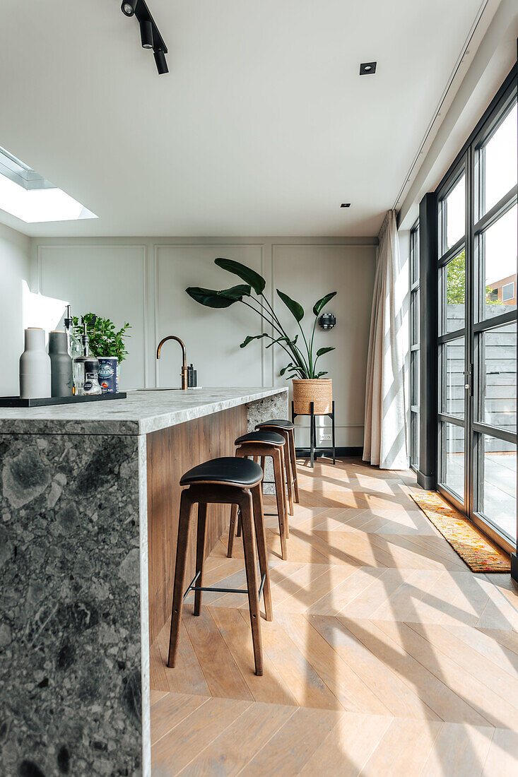 Modern kitchen with marble worktop, wooden bar stools and large wall of windows