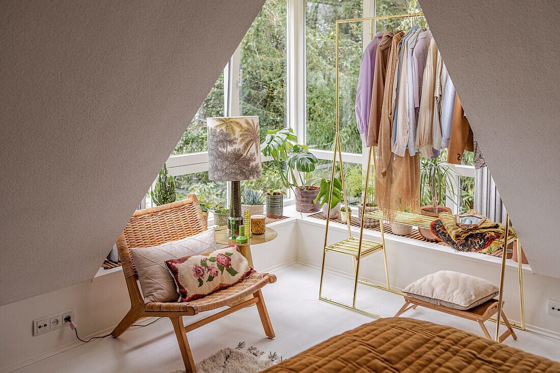 Bright bedroom with sloped ceiling, wardrobe, rattan chair and plants