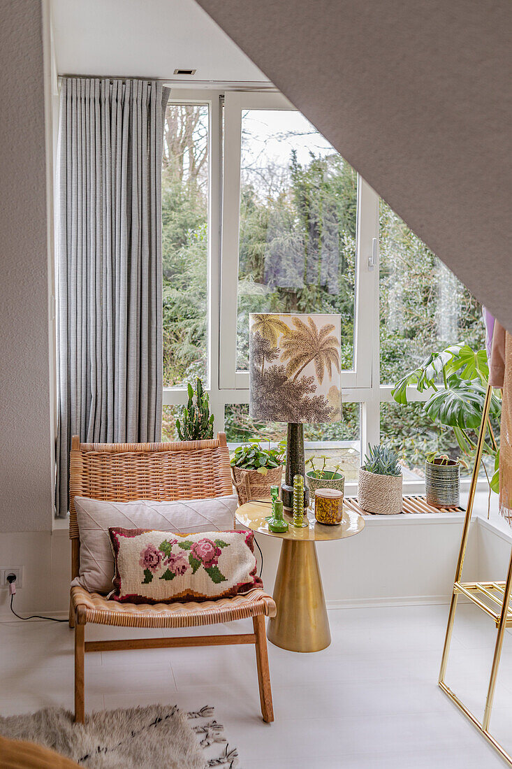 Sitzbereich mit Rattanstuhl und Pflanzen vor großem Fenster