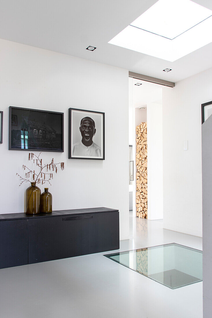 Modern hallway with glass floor, black sideboard and art portraits on the wall