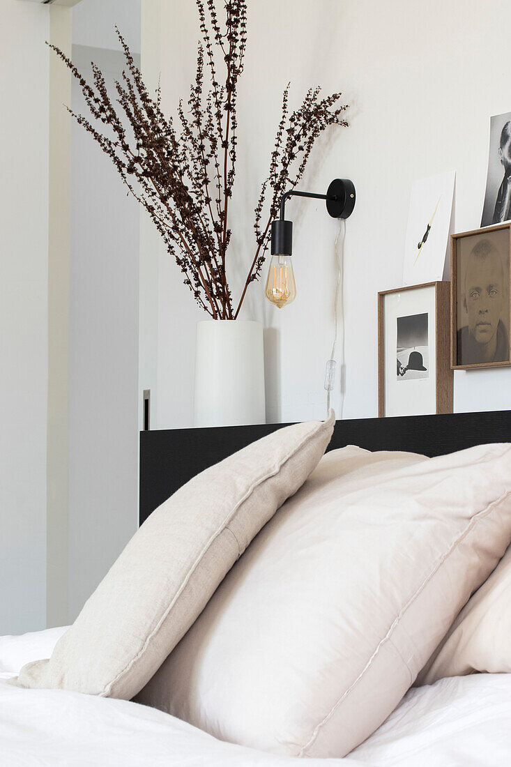 Bedroom with black headboard, wall lamp and dried flower vase