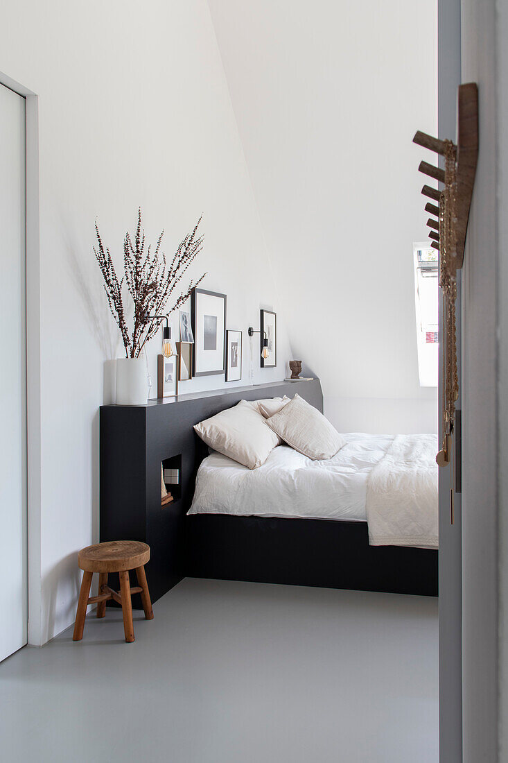 Bedroom with black bed headboard, white walls, picture wall and wooden accessories