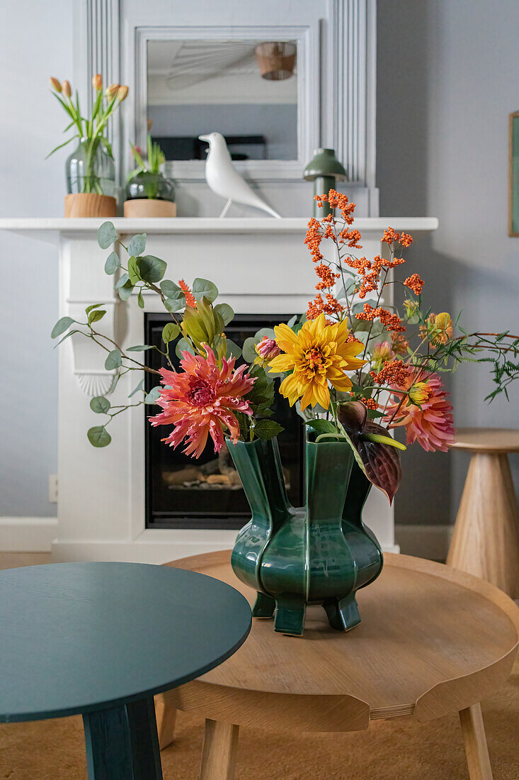 Blumenarrangement mit Dahlien und Eukalyptus in grün glasierter Vase auf Holz-Couchtisch