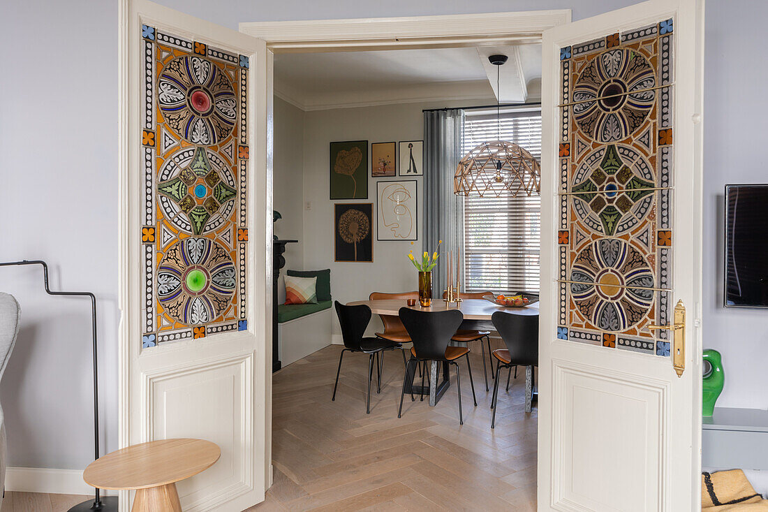 View through stained glass double doors into dining room with wooden dining table and black chairs