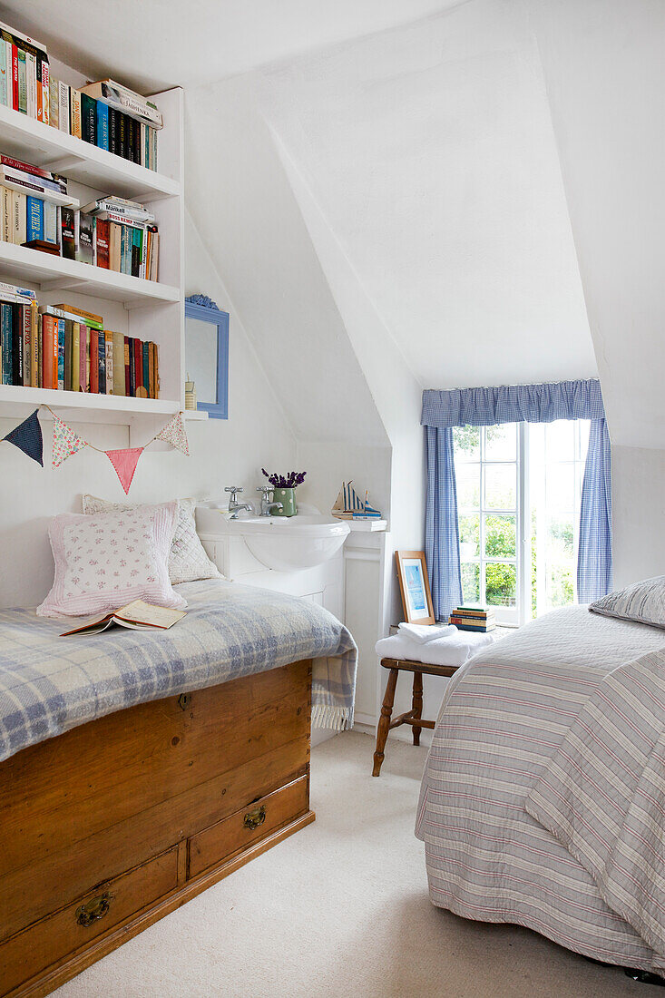 Attic bedroom with built-in bookshelf, bench and blue curtains