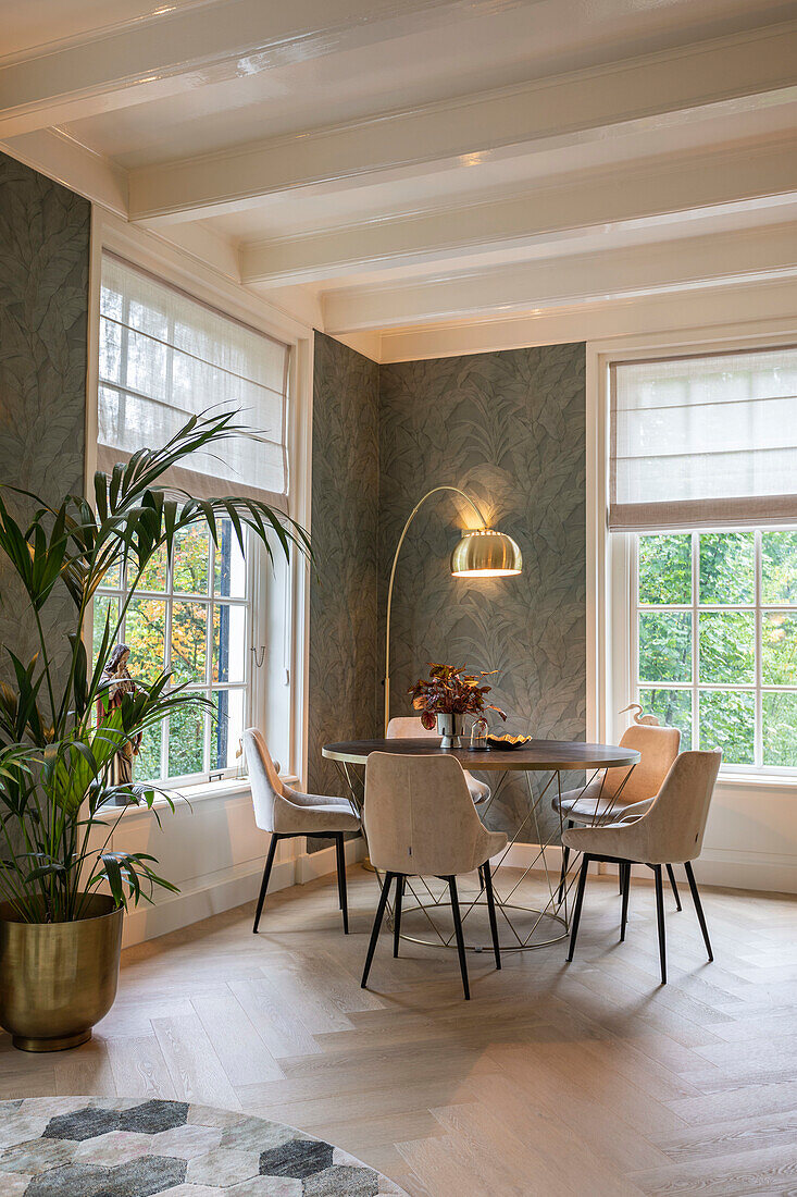 Modern dining area with round table and upholstered chairs in front of large windows