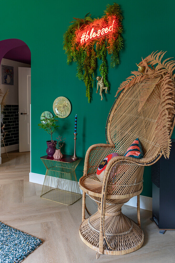 Rattan-Hochlehnsessel und goldener Beistelltisch vor grüner Wand mit Neon-Schild "blessed"