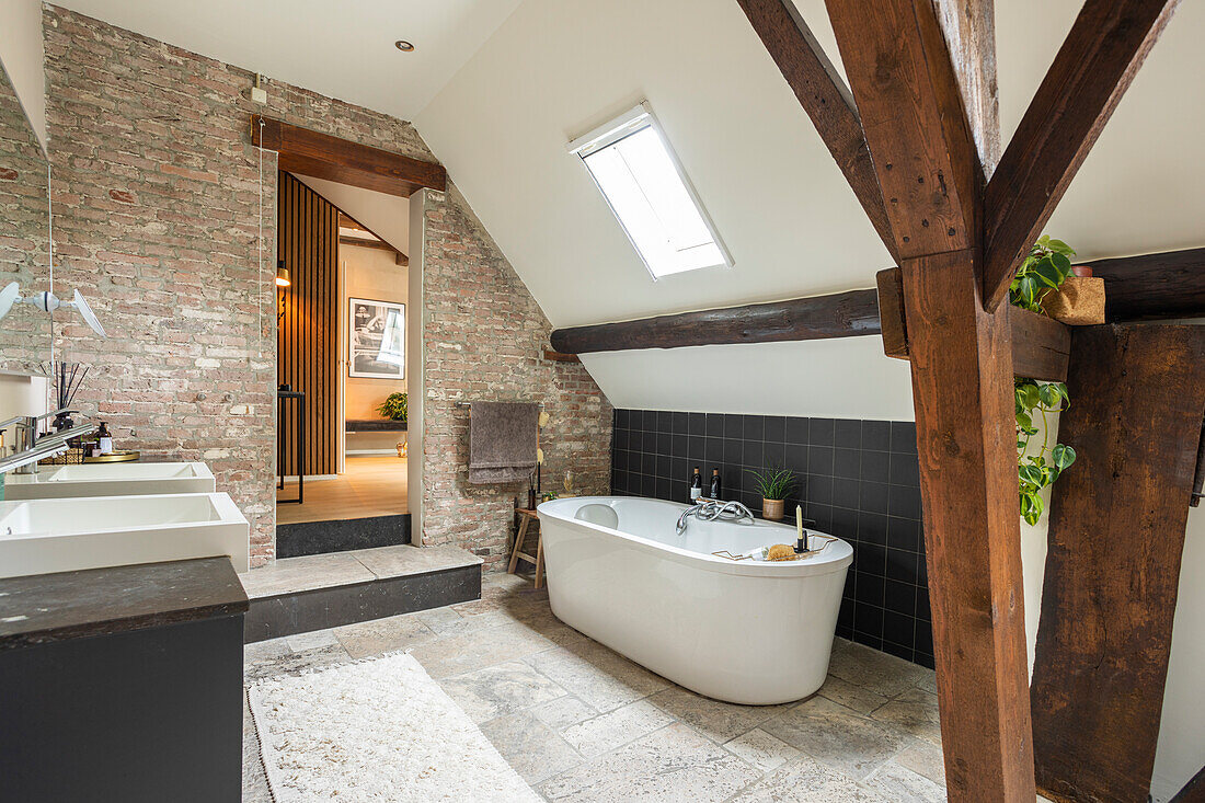 Free-standing bathtub in modern bathroom with brick walls and sloping roof