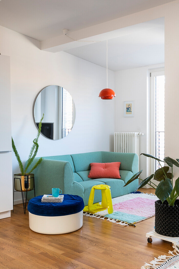 Living area with turquoise sofa, round mirror and colourful decoration