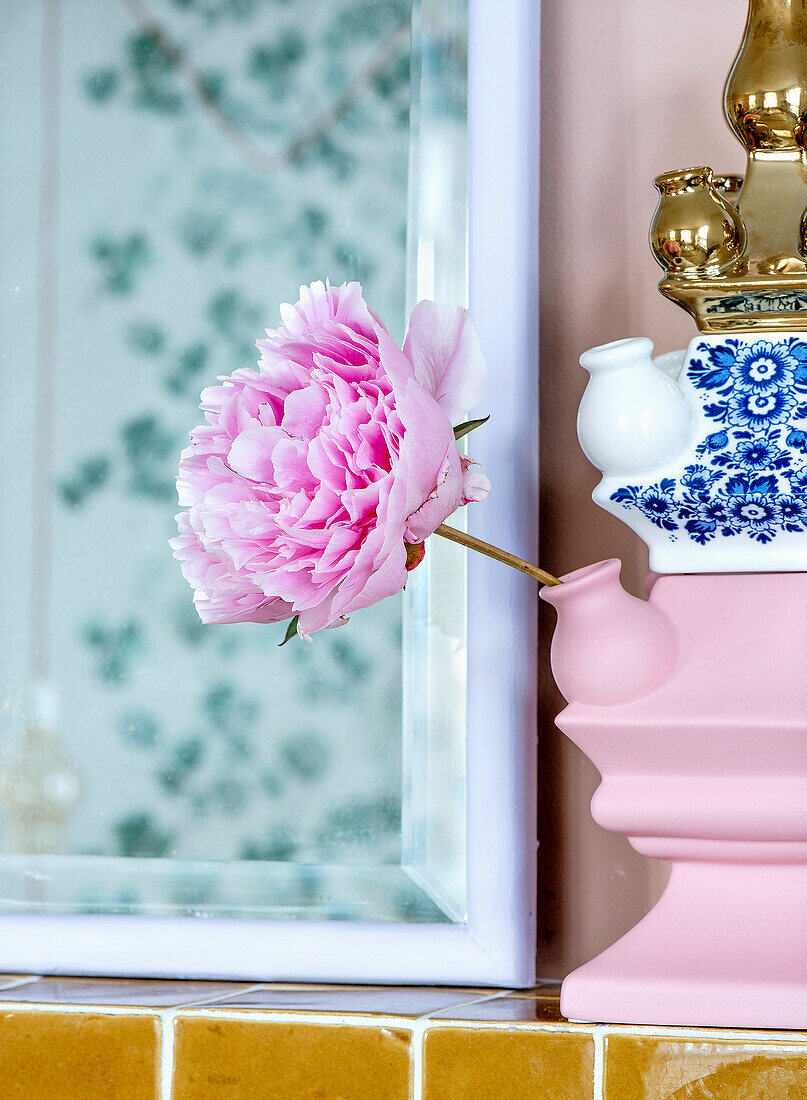 Single pink peony in unusual vase in front of mirror