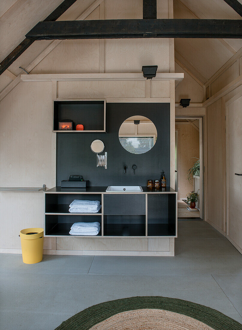 Washbasin with black splashback and round mirror in modern bathroom