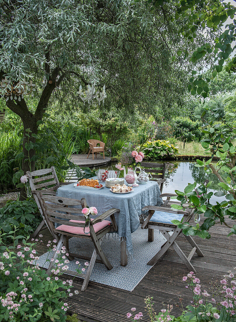 Wooden table set with flowers and pasties by the pond