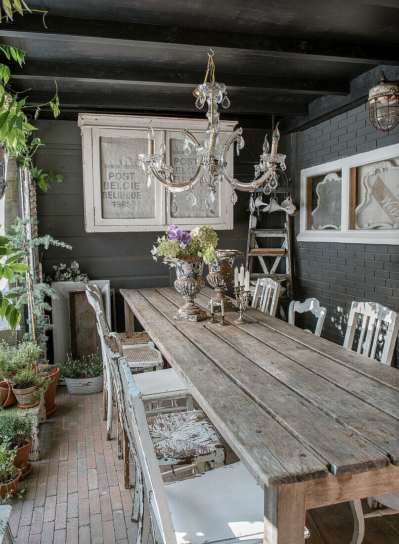 Long wooden table with chandelier and vintage decorations on a covered terrace