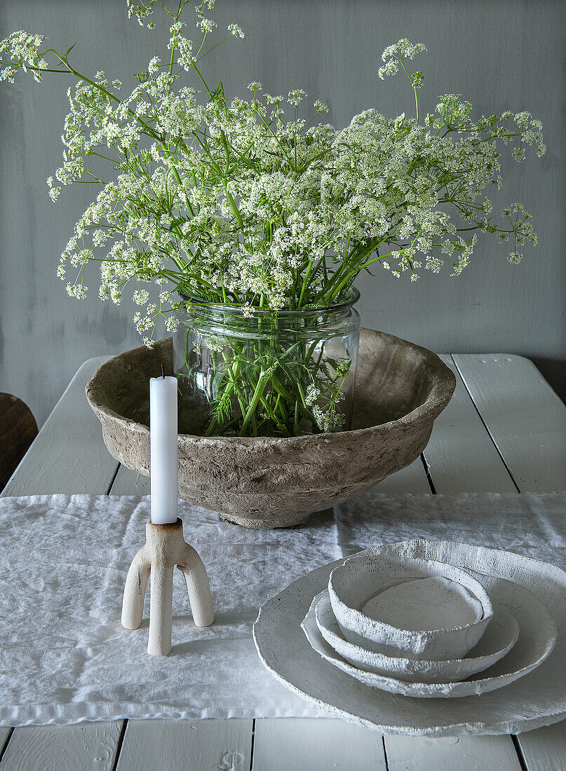 Gedeckter Holztisch mit Kerzenhalter, Schalen und Blumenvasenarrangement