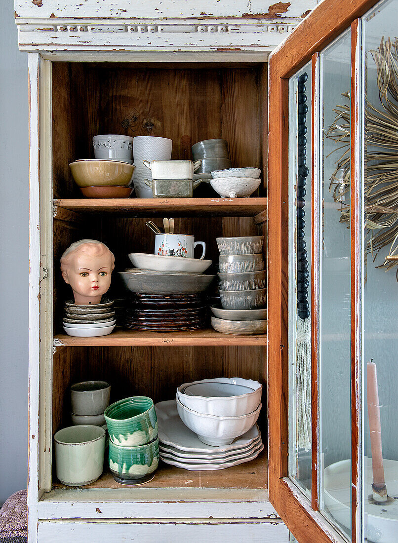 Alter Geschirrschrank mit Vintage-Keramik und Puppenkopf