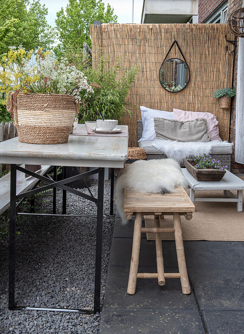 Gemütliche Sitzecke mit Naturmaterialien auf der Terrasse, Blumenarrangement im Korb