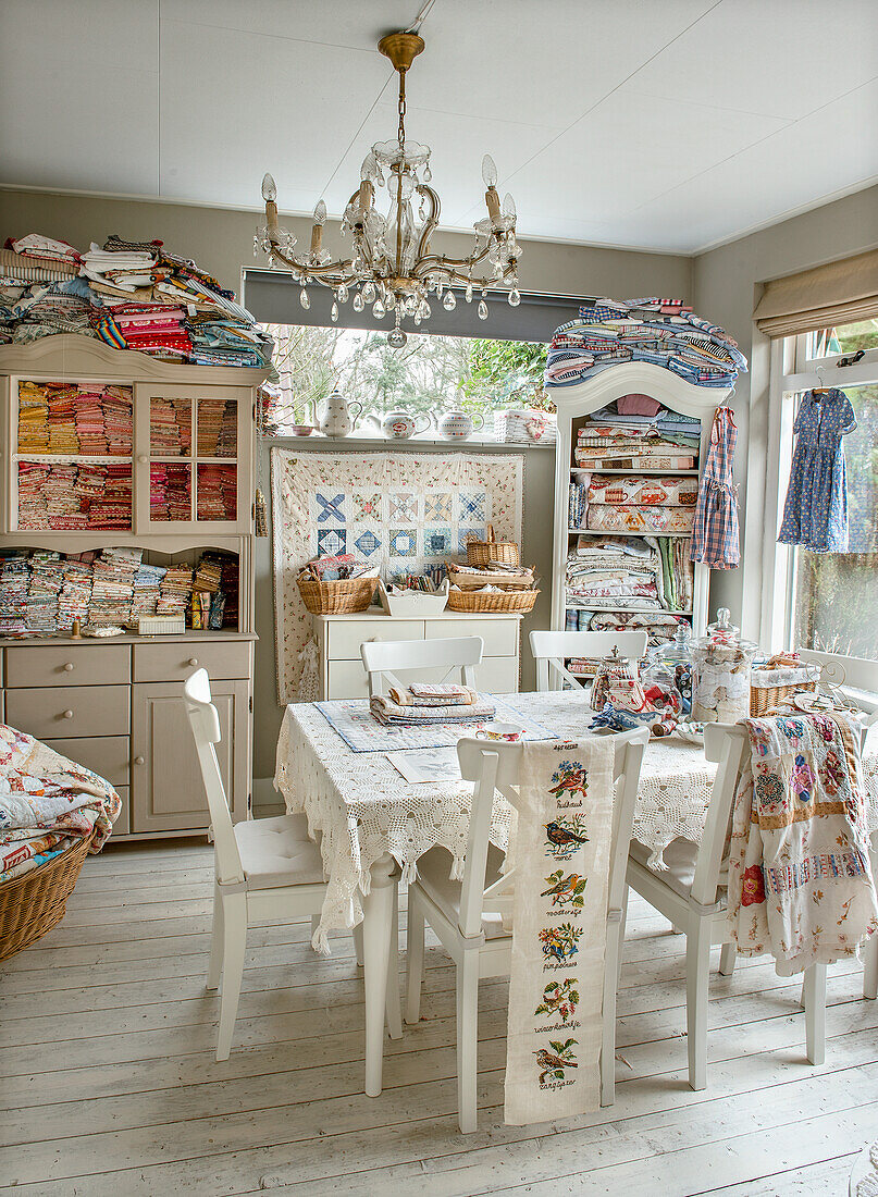 Bright sewing room with cupboards and chandelier and assorted fabrics