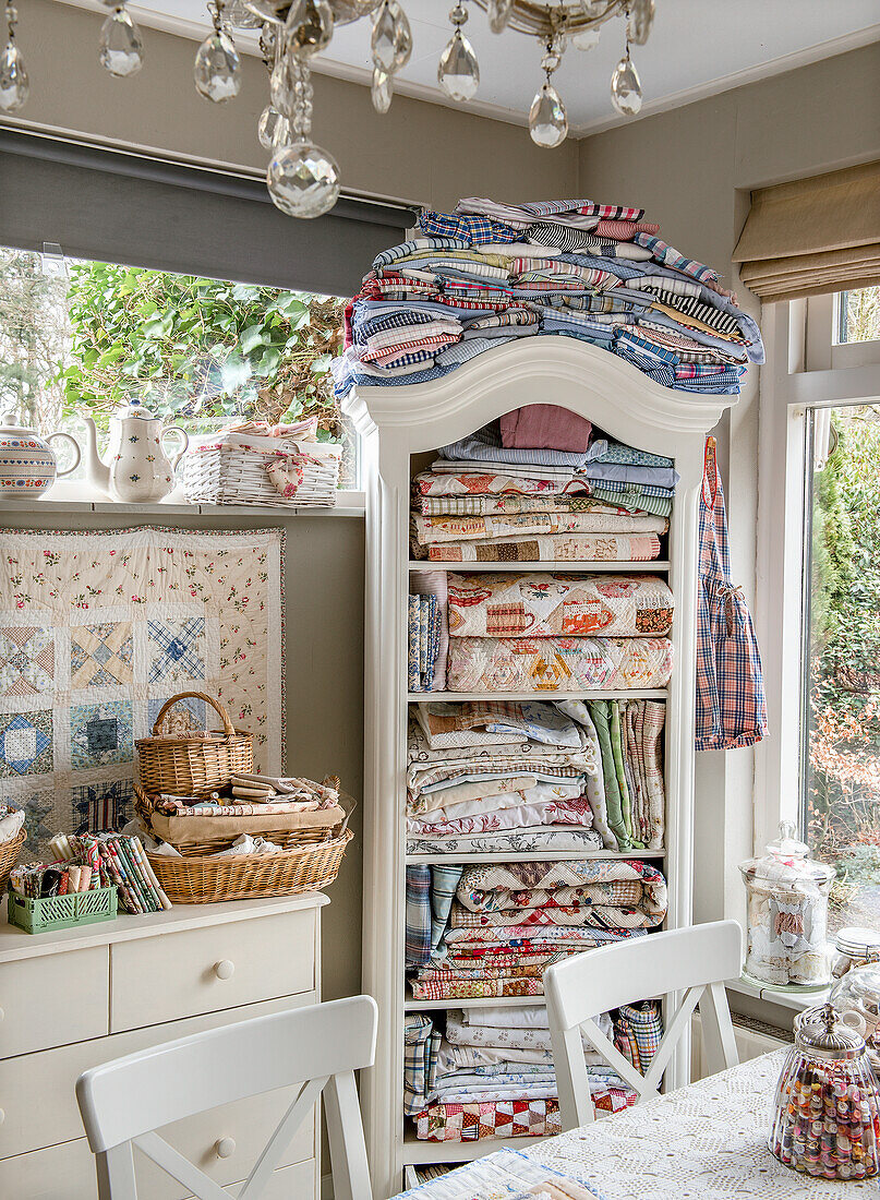 Sewing room with antique cupboard full of colorful, patterned blankets, fabrics and scarves