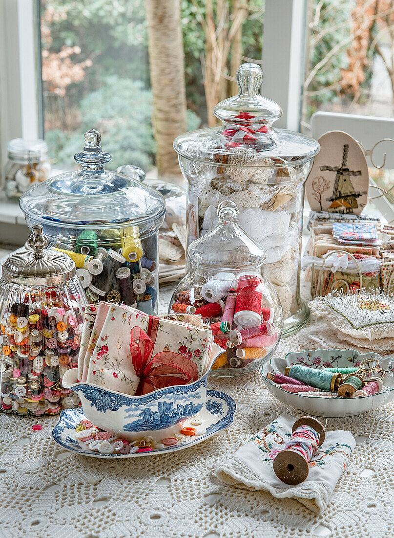 Nähutensilien im Vintage-Look mit Garnrollen und Stoffen in Glasbehältern auf Häkeldecke