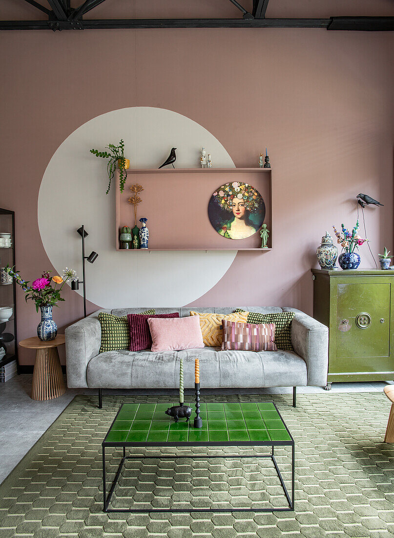 Wohnzimmer mit rosa Wand, grünem Fliesentisch und grauem Sofa