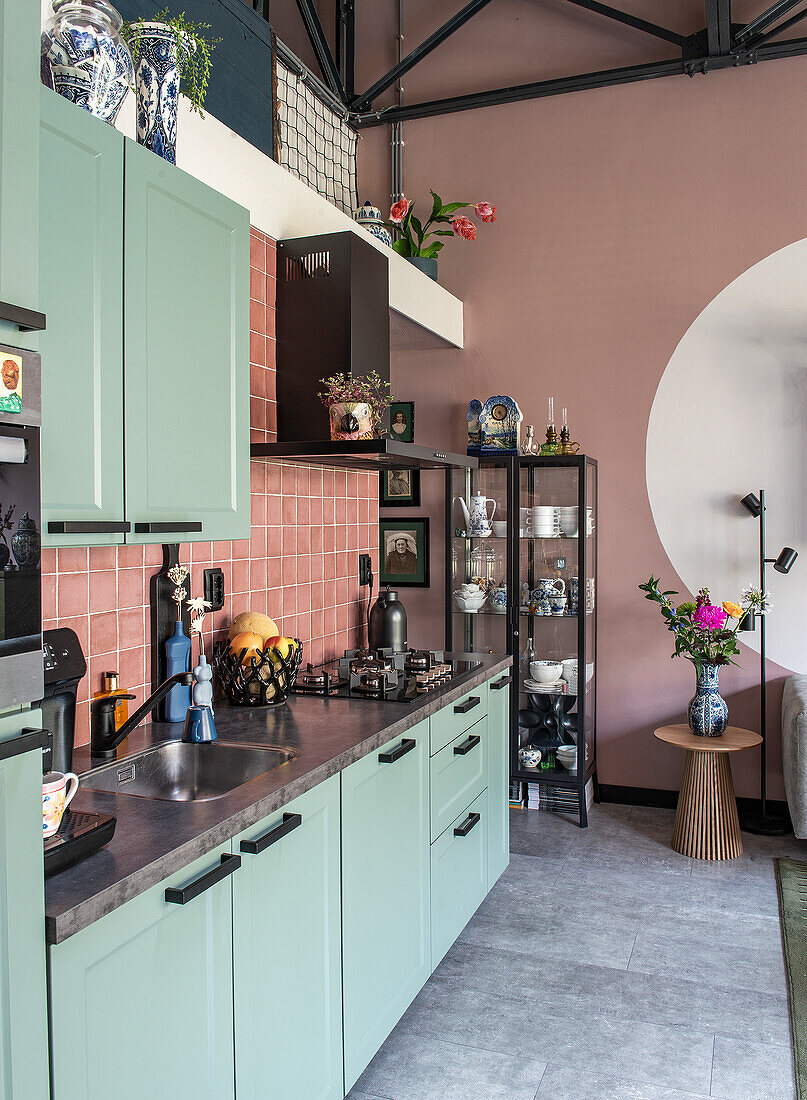 Kitchen with mint green cupboards, pink tiles and metal shelving