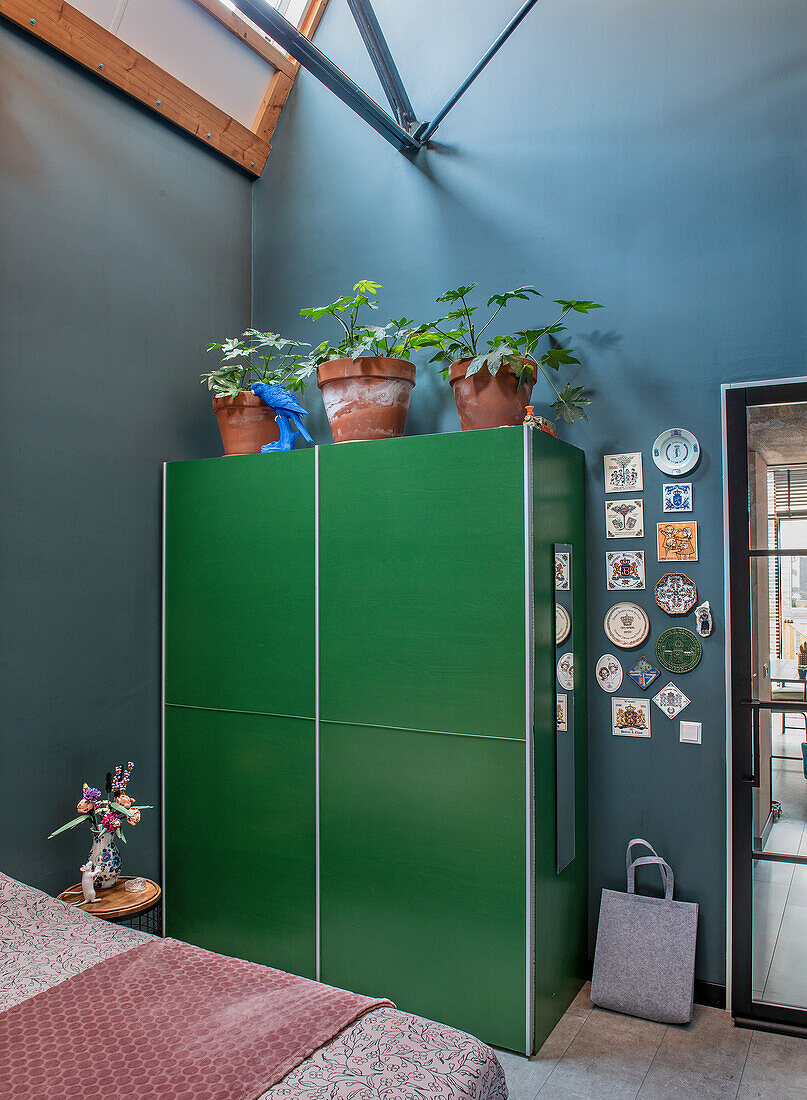 Green wardrobe with houseplants and wall decorations in a modern bedroom