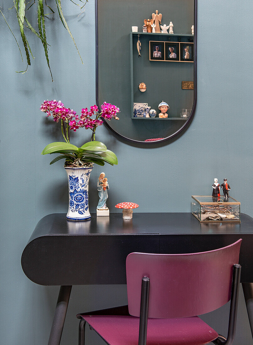 Black table with orchid in blue and white vase, pink chair