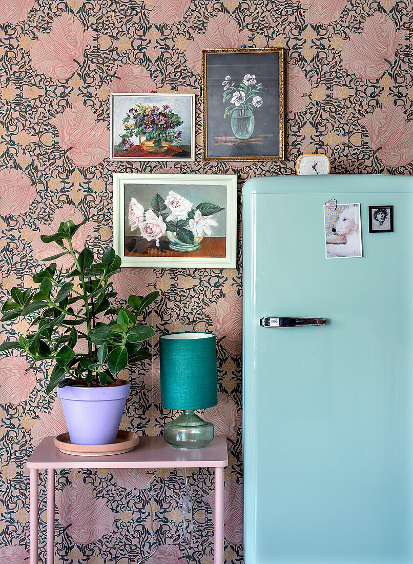 Retro fridge and plant in front of floral wallpaper and flower pictures