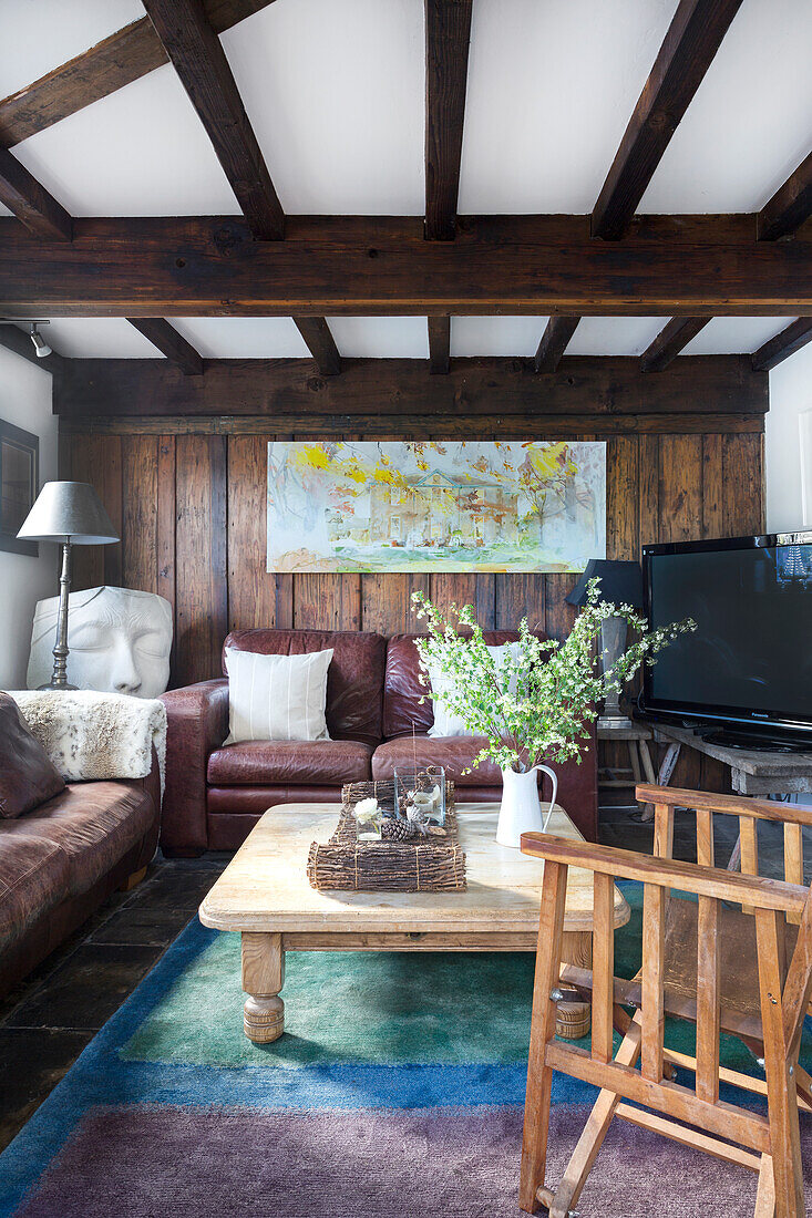 Cozy living room with wooden beamed ceiling, leather sofas and rustic coffee table