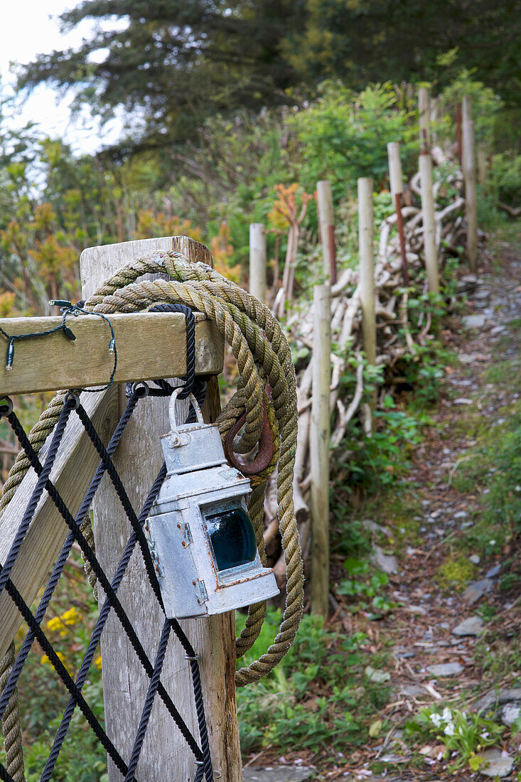 Laterne und Seil an einem Holzzaun entlang eines Wanderweges im Wald