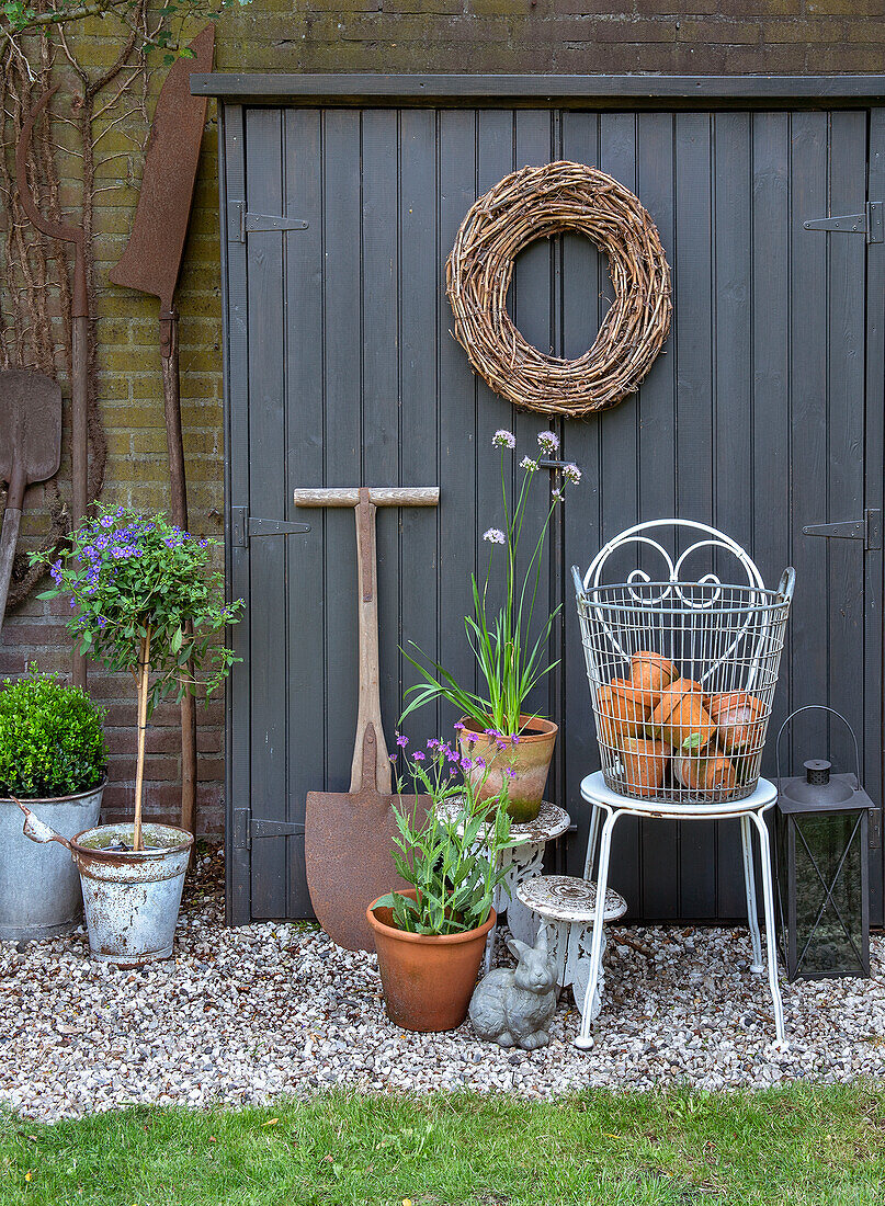 Garden shed with decorative wreath, zinc pots, clay pots and cast iron chair