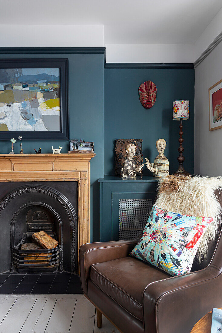 Brown leather armchair with patterned cushion in front of fireplace and assorted art on the wall