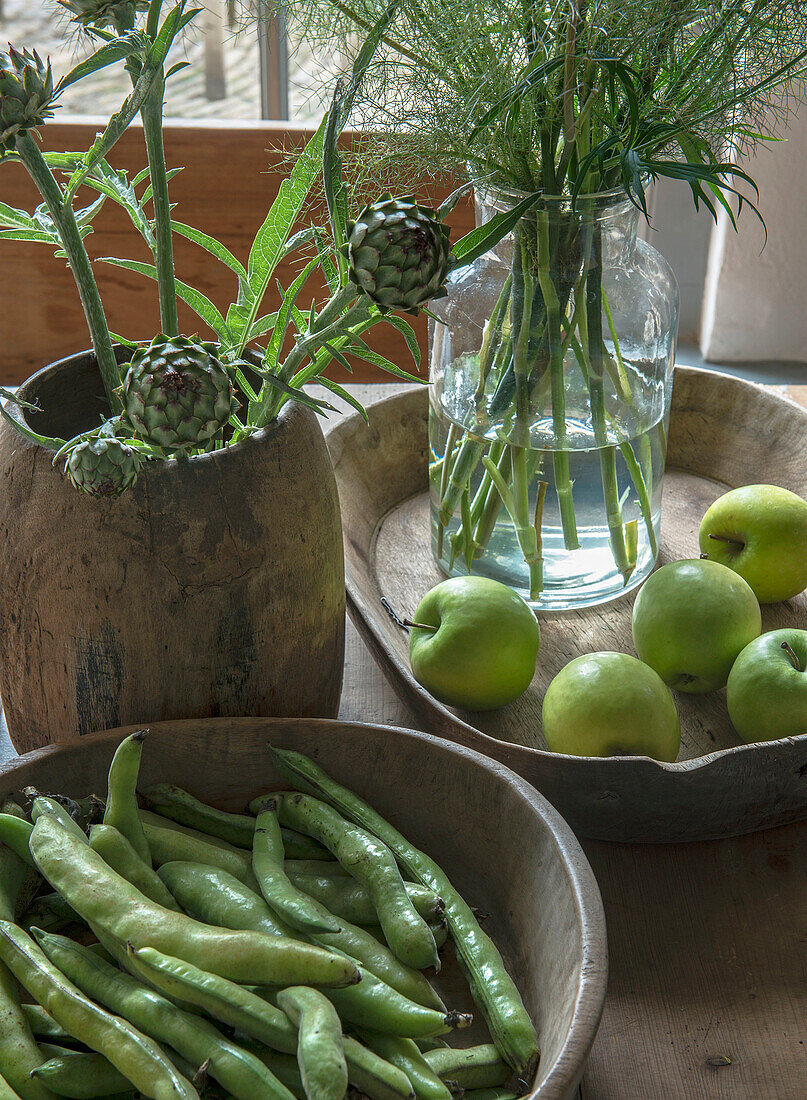 Artichokes, green apple, and beans in wooden bowls on wooden table