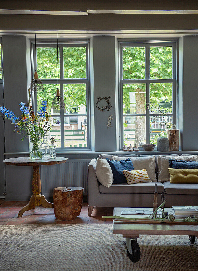 Living room with large windows, corner sofa and round side table with bouquet of flowers