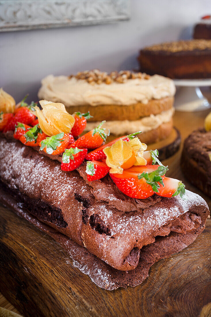 Chocolate sponge roll with strawberries and physalis on a wooden plate