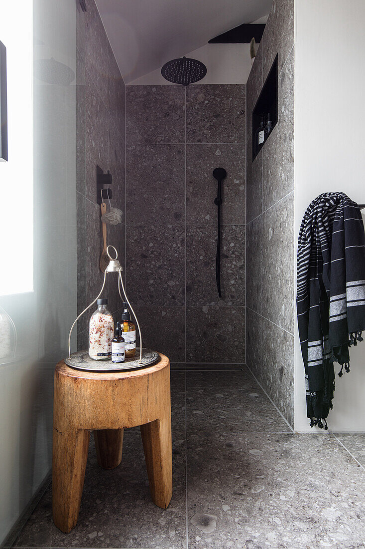 Shower corner with grey tiles and wooden accents in a modern bathroom